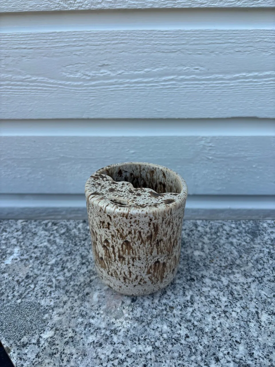 Bägare i beige lera med kraterformad, grovt spräcklig glasyr.