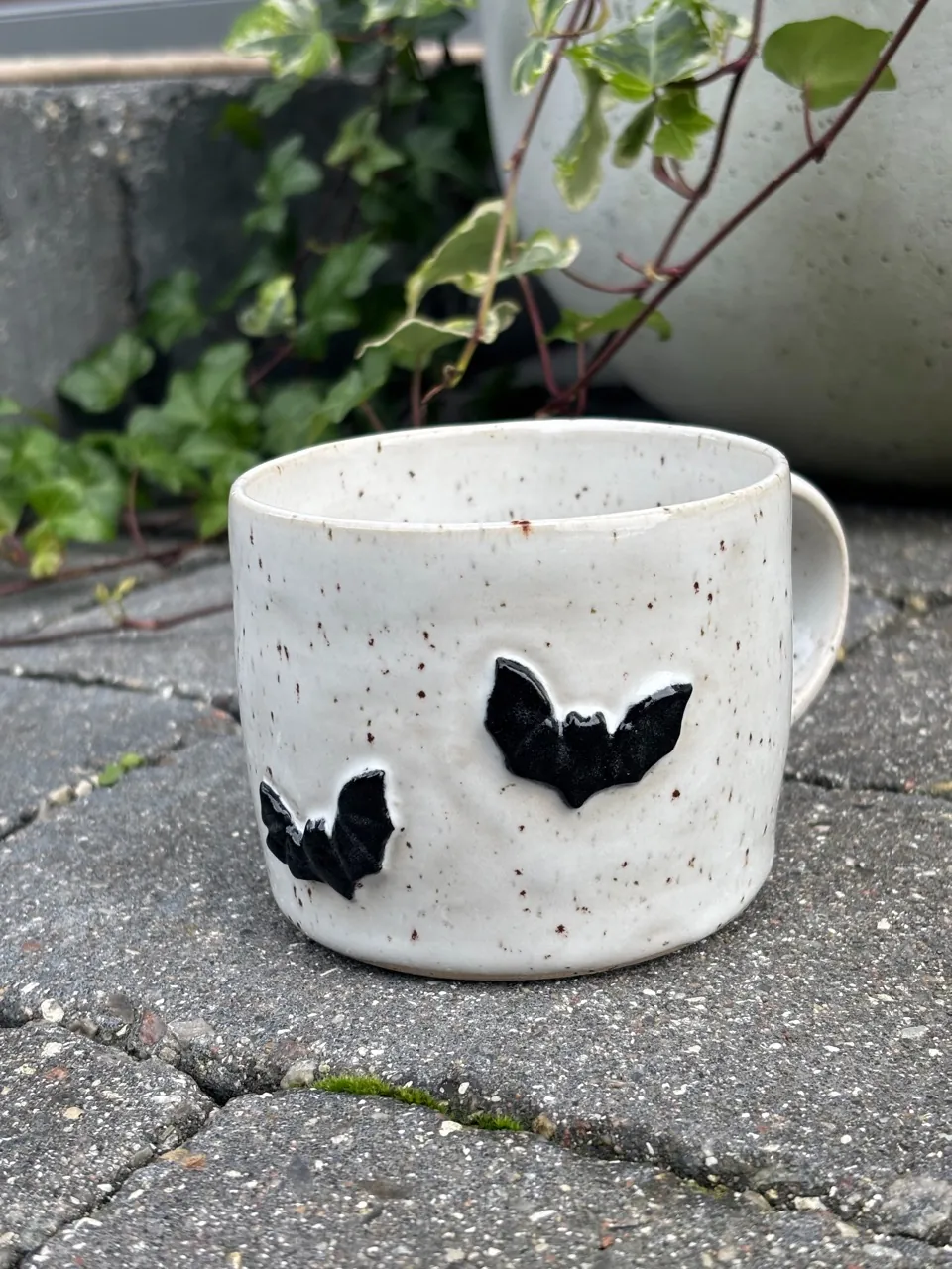 Vit spräcklig mugg med två svarta fladdermöss pålagda på sidan.