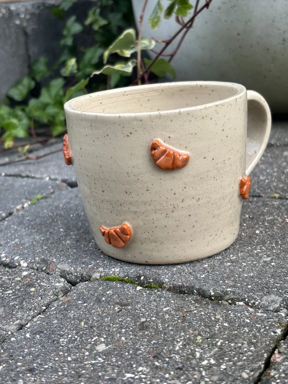 Ljus spräcklig mugg med öra och orangeröda croissanter pålagda runt sidan.